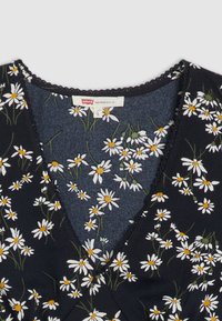 Robe florale avec un fond bleu marine, ornée de marguerites blanches aux centres jaunes, col en V, et une délicate bordure festonnée.