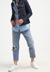 Granatowa kurtka dżinsowa, lekką niebieską koszulę pod spodem, przetarte jasnoniebieskie dżinsy z podwiniętymi nogawkami oraz białe trampki.