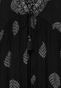 Tissu noir avec motifs de feuilles blanches, muni d'un cordon tressé avec pompons à un col froncé avec des détails brodés.