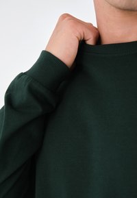 Grønn bomullshettegenser med ribbefestet rund hals og lange ermer, med en myk tekstur og en tettsittende design.