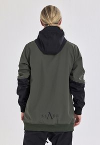 Grøn og sort hættetrøje med løs pasform, der har et logo på ryggen, elastiske manchetter og en glat tekstur.