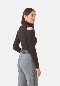 Jersey negro con cuello alto y cortes en los hombros. Combinado con pantalones grises que presentan bordados intrincados a lo largo de los costados y un cinturón negro.