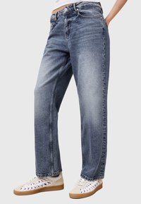 Jeans celesti, a vita alta e dal taglio rilassato, con zone sbiadite, cinque tasche e una chiusura con bottone classica. Indossati con sneakers bianche.