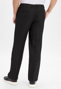 Schwarze Hosen mit einem elastischen Bund, zwei Gesäßtaschen, schmal zulaufenden Beinen und einer glatten Textur, kombiniert mit schwarzen Sneakers und weißen Sohlen.
