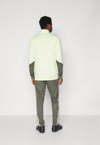 Light green sports jacket with dark green accents, zip collar, and long sleeves. Paired with dark green pants featuring side stripes.