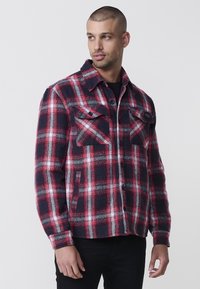 Punane ja must ruuduline flanellshirt, millel on nööbid ees, kaks rinnataskut ja lühendatud disain. Pehme tekstuur ja klassikaline stiil.