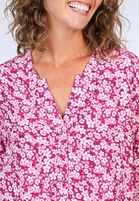 Flower-patterned top in vibrant pink with white floral designs. Features a V-neckline and short sleeves, made from light, textured fabric.