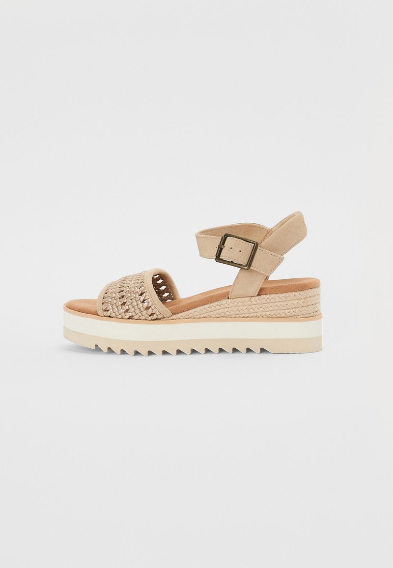 Beige wedge sandal with woven design, adjustable ankle strap, and textured platform. Features a sturdy sole with zigzag pattern.