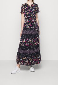 Maxiklänning med en mörk marinblå tyg med flerfärgade blommönster, korta ärmar, en nyckelhålsknäppning och en flerlagrig volangärmsfåll.