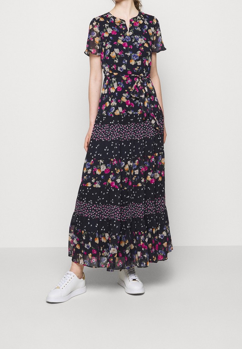 Maxiklänning med en mörk marinblå tyg med flerfärgade blommönster, korta ärmar, en nyckelhålsknäppning och en flerlagrig volangärmsfåll.