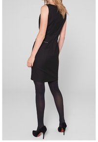 Svart ärmlös klänning med en figursydd silhuett, med sid sömmar och dragkedja som dekoration. Matchas med genomskinliga svarta strumpbyxor och ankelklackar.