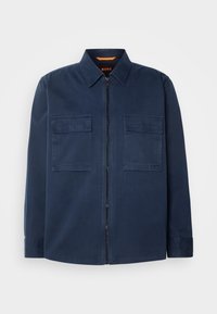Veste bleu marine zippée avec col et deux poches poitrine à rabat, affichant un logo subtil "BOSS" sur la poche gauche.
