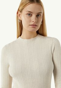 Jasno beżowy sweter z prążkowanego dzianiny z falbaniastym dekoltem i textured wzorem, z długimi rękawami i dopasowanym krojem.