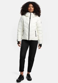 White, puffy jacket with a high collar, black zipper, and side pockets, paired with black pants and sneakers. Textured fabric with a quilted design.