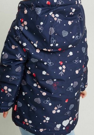 Barn iført mørkeblå jakke med hætte, dekoreret med pink og hvide blomster, sommerfugle, hjerter og røde mariehøns.