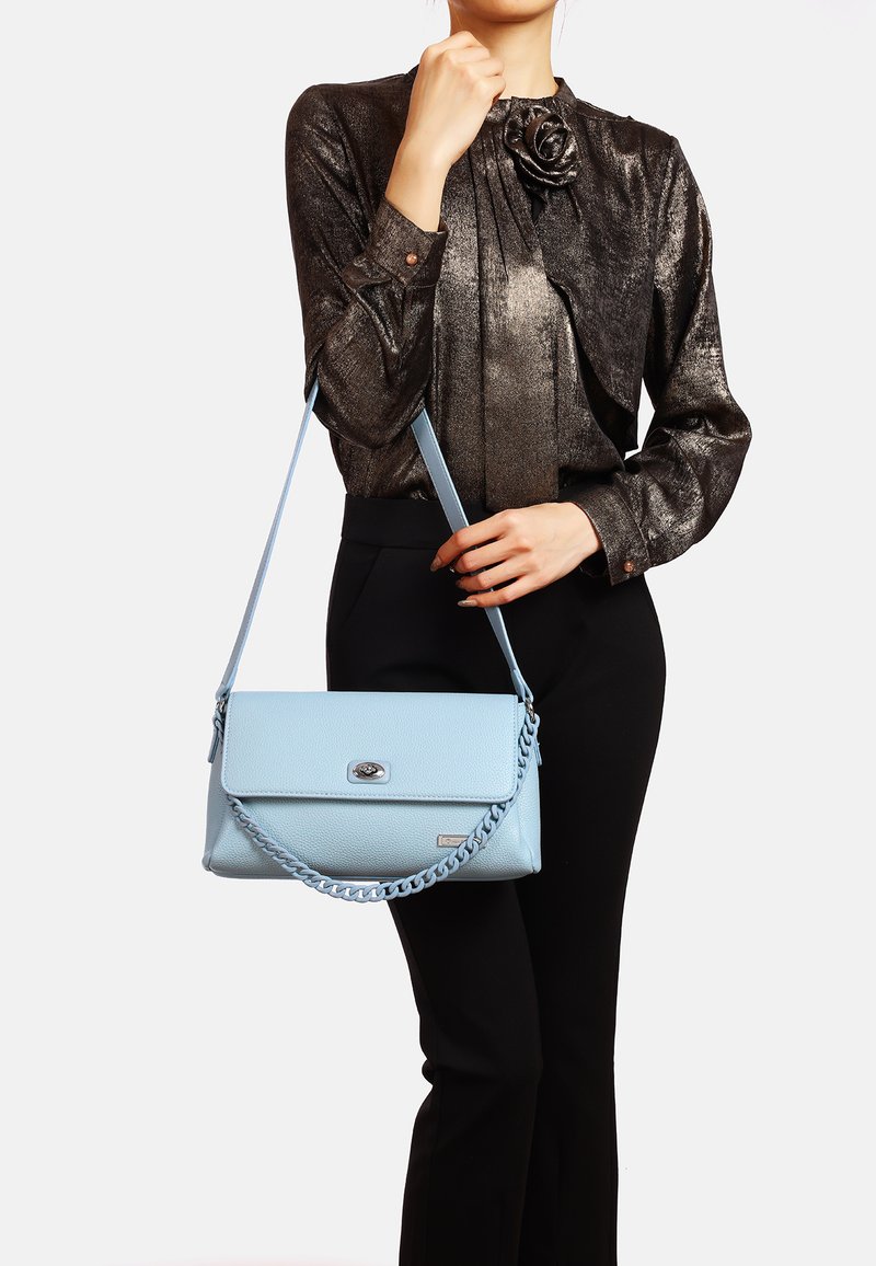 Borsa a mano in pelle blu chiaro con una finitura texture, dotata di una tracolla a catena e una chiusura a bottone argentato, tenuta da una persona in abbigliamento scuro.