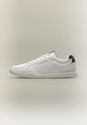 Sneaker bianco basso con lacci, logo Tommy Hilfiger sul lato, linguetta nera sul tallone e suola testurizzata su sfondo semplice.