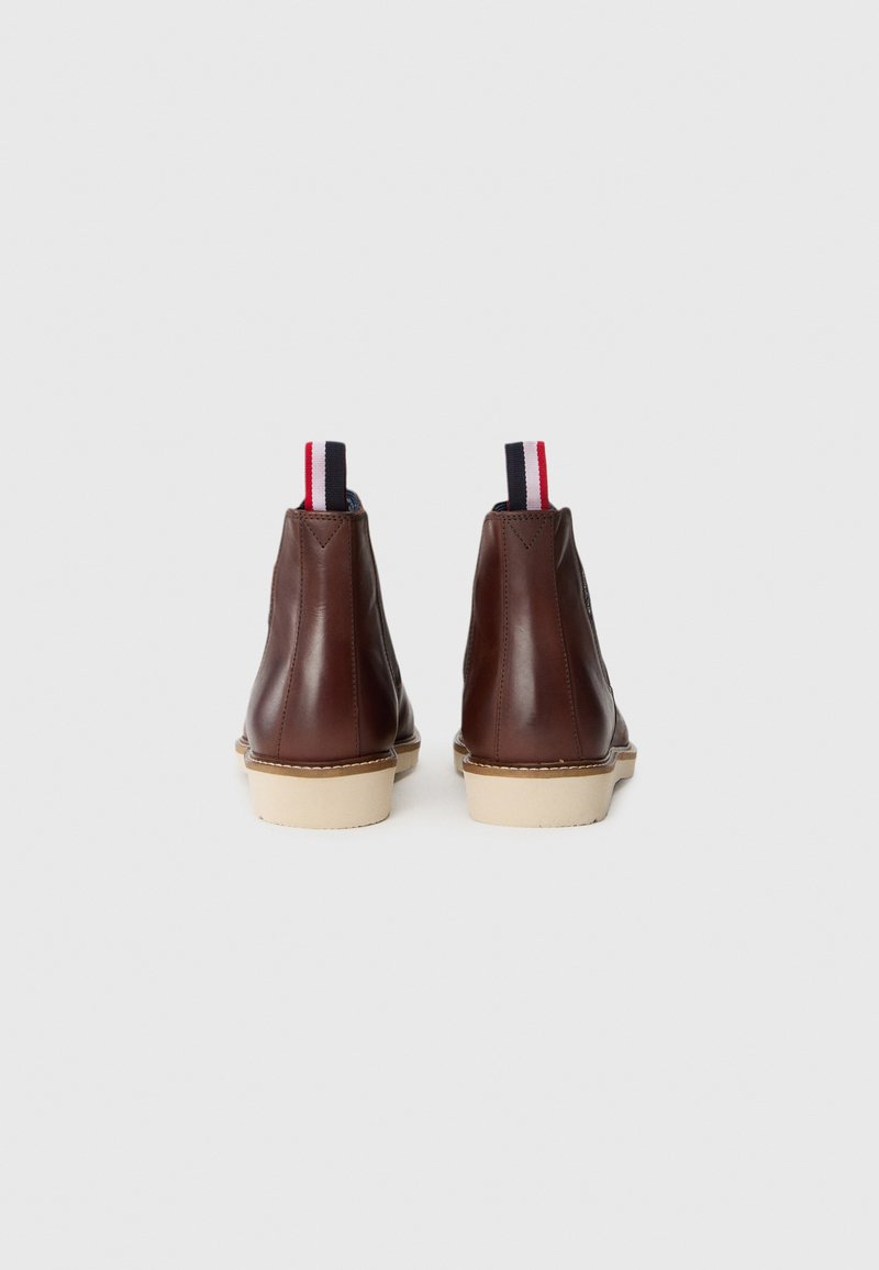 Bottines en cuir marron avec une forme arrondie, semelles beige, et brides en tissu contrasté avec des rayures rouge, blanc et bleu.