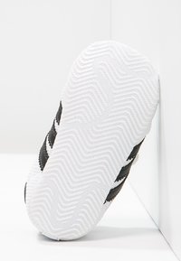 Svartvit sportskosula med ett strukturerat mönster i vitt gummi, böjd form och svarta randiga detaljer.