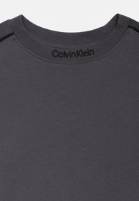 Γκρί βαμβακερή μπλούζα T-shirt με στρογγυλή λαιμόκοψη, με μαύρη επωνυμία στον γιακά και διακοσμητικές λεπτομέρειες στα πλαϊνά. Λείο ύφασμα, άνετη εφαρμογή.