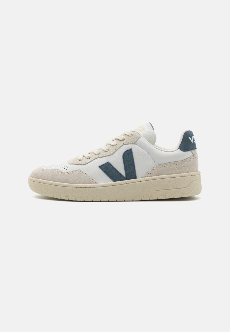 Witte leren sneakers met grijze suède accenten, voorzien van een opvallend blauw "V"-logo, ronde neus en een gestructureerde rubberen zool.