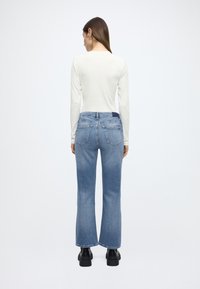 Lichtgekleurde top met lange mouwen gecombineerd met blauw, uitgespreide jeans met een normale taillehoogte. De jeans hebben een ontwerp met vijf zakken en zichtbare stikseldetails.