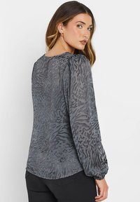 Blusa grigia con stampa animale, in tessuto texturizzato, maniche lunghe a sbuffo e scollatura rotonda. Presenta un polsino elastico per un look aderente.