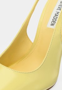 Κίτρινο παπούτσι με τακούνι από λείο δέρμα με γυαλιστερή όψη, με κομψό σχεδιασμό, επιμηκυμένη στρογγυλεμένη μύτη και λείο φινίρισμα, αποκαλύπτοντας λεπτομέρειες της εσωτερικής επένδυσης.