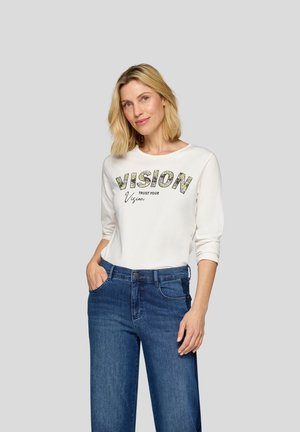 Helles, langärmliges Shirt mit "VISION" Grafik, kombiniert mit dunkelblauen, weit geschnittenen Jeans. Glatte Stofftextur, runder Halsausschnitt, lässige Passform.