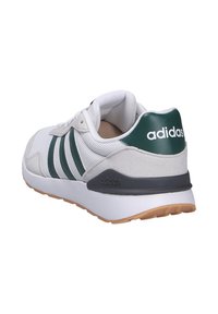 Zapatilla blanca con detalles verdes, parte superior de ante texturizado y malla. Presenta tres rayas verdes y una suela de goma. La parte trasera tiene el logo.