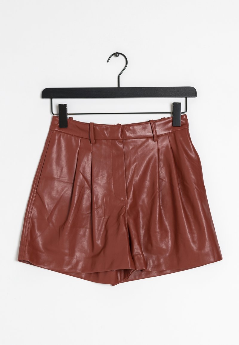 Rdzawopomarańczowe skórzane szorty o gładkiej teksturze, z plisami, dopasowaną talią i standardowym dołem, wiszące na czarnym wieszaku.