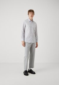 Light grey button-up shirt with vertical white stripes, paired with light grey trousers. Black loafers and white socks complete the outfit.