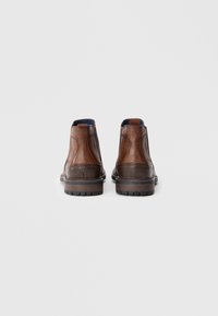 Bruine leren enkelboots met een gladde textuur, een ronde neus en een lage gestapelde hak. Beschikt over elastische zijpanelen en een blauwe binnenvoering.