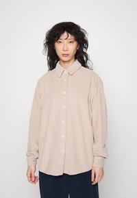 Camicia in corda beige con chiusura a bottoni, texture morbida e colletto, con maniche lunghe e taglio rilassato.