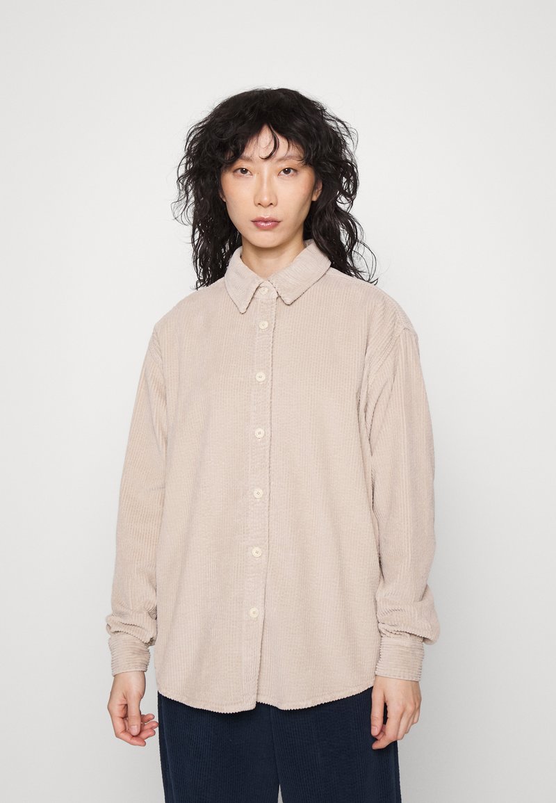 Camicia in corda beige con chiusura a bottoni, texture morbida e colletto, con maniche lunghe e taglio rilassato.