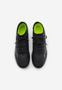 Czarne buty sportowe z teksturowaną cholewką, żółtymi wkładkami i żebrowanym wzorem. Posiadają tradycyjne sznurowadła i białe logo z boku.