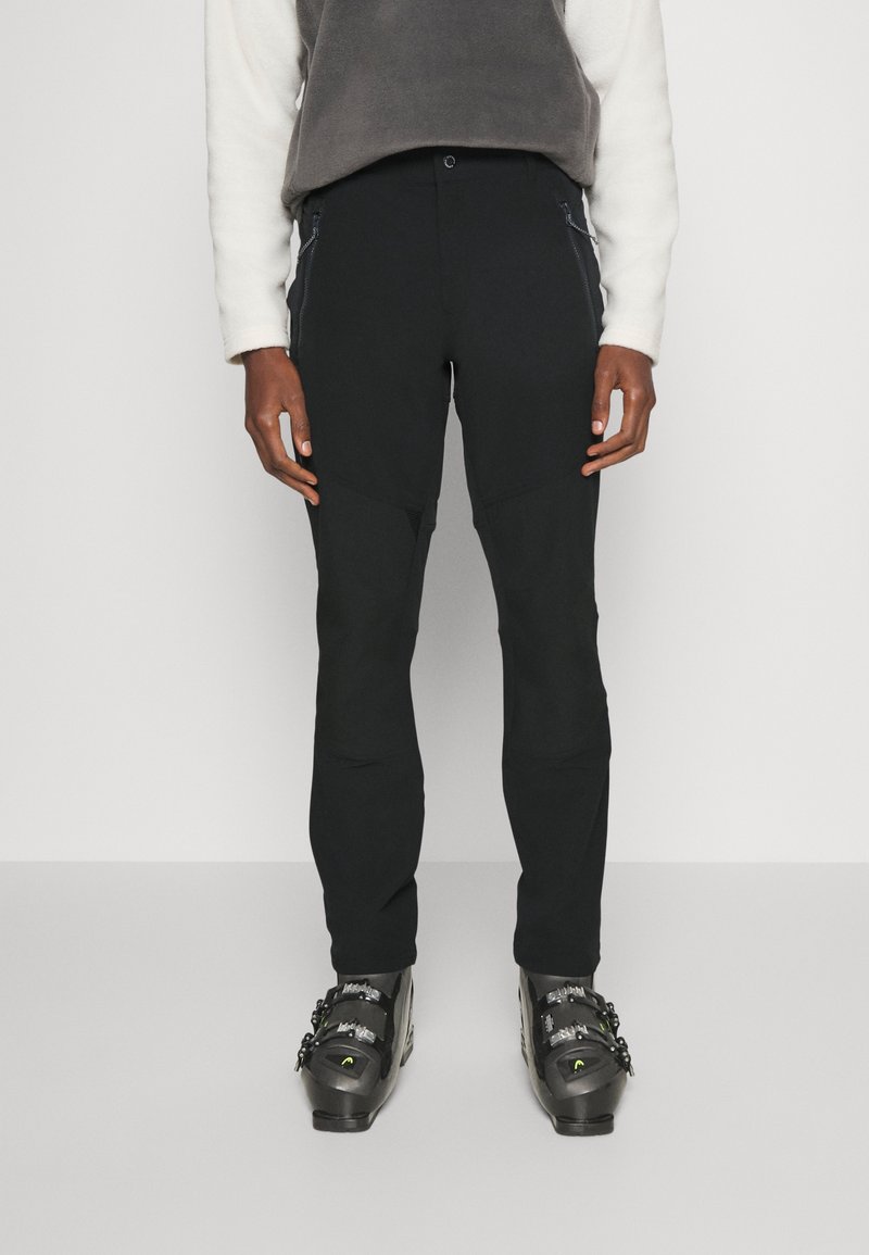 Musta kiipeilyhousut, joissa on slim fit -leikkaus, vahvistetut polviosat ja vetoketjulliset taskut. Yhdistetty mustiin hiihtobootseihin ja vaaleanharmaaseen fleecepaitaan.