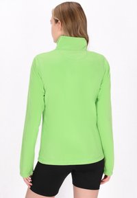 Grøn fleecetrøje med høj krave, lange ærmer og en blød tekstur. Den er parret med sorte shorts. Simpelt design uden mønstre.