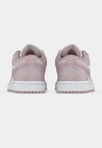 Baskets en daim rose avec accents blancs, présentant un col rembourré, le logo Air Jordan au talon et une semelle en caoutchouc texturée avec un profil de bande de roulement visible.