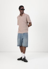Stribet kortærmet polo shirt i brun og hvid, parret med lyseblå denim shorts. Sorte sko og solbriller fuldender outfittet.