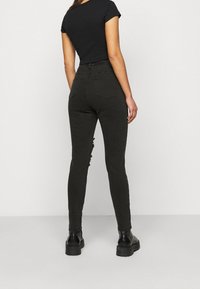 Jeans skinny negros de tiro alto con detalles desgastados en el muslo izquierdo, combinados con una blusa ajustada negra de manga corta y botas negras gruesas.