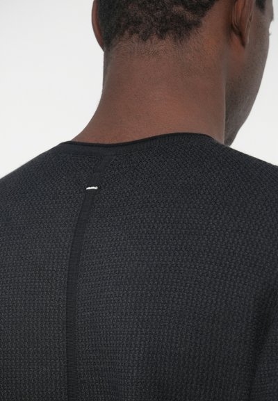 Black textured sweater with a round neckline, featuring a contrasting white stitch detail at the back seam. Clean and minimal design.