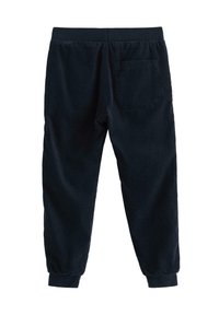 Mørkeblå corduroy joggerbukser med elastisk talje, manchetter ved anklerne og en baglomme. Stoffet har et blødt, tekstureret look.