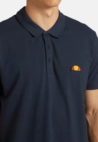 Polo shirt blu navy in cotone con colletto, patta con tre bottoni e un piccolo logo ricamato in rosso e giallo.