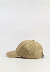 Beżowa czapka baseballowa z zakrzywionym daszkiem, teksturowana tkanina i tłoczony wzór fal na boku. Regulowany pasek z tyłu.