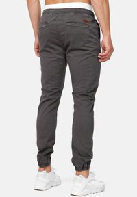 Pantalones jogger de algodón grises con cintura y puños elásticos, que cuentan con dos bolsillos traseros y una etiqueta de acento de cuero marrón.