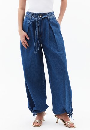 Hoge taille, losse blauwe jeans met een geweven riem, voorzien van zijzakken en verstelbare manchetten met veters bij de enkels.