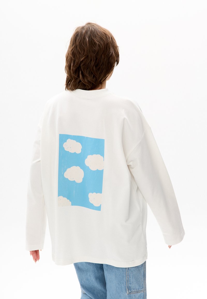 Sweatshirt blanc oversize avec un graphique carré bleu représentant des nuages blancs au dos. Coupe ample avec épaules tombantes, texture douce.