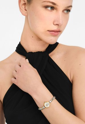 Gold-tone watch with a white face and silver beads. Bracelet style features alternating clear and black stones, set against a black fabric background.