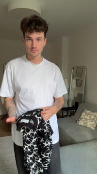 Μαύρη και άσπρη ζακέτα με σχέδιο που κρατιέται στα χέρια ενός ατόμου. Η ζακέτα διαθέτει μαύρο γιακά και αφηρημένο σχέδιο σε υφασία με υφή.